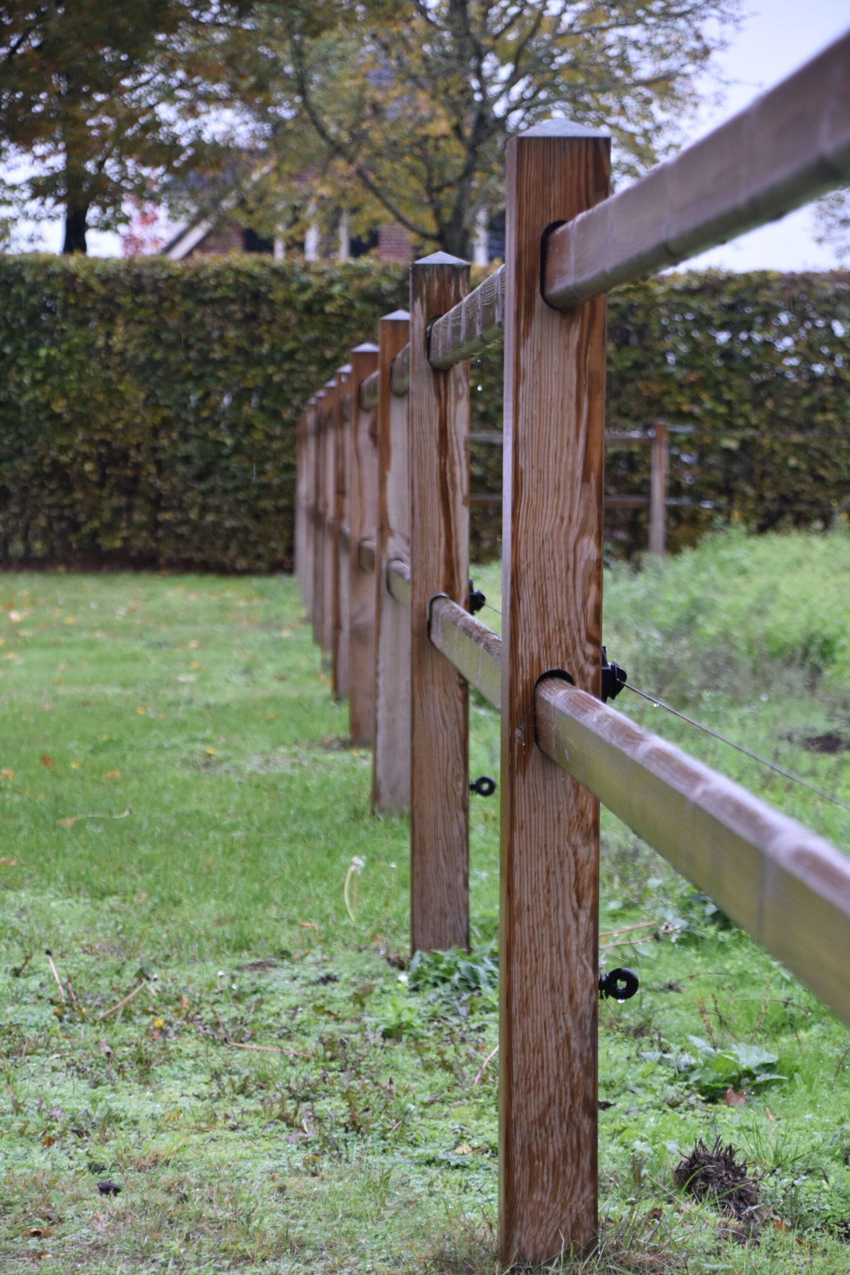 A perspective view of a wooden fence in a green field under a cloudy sky.