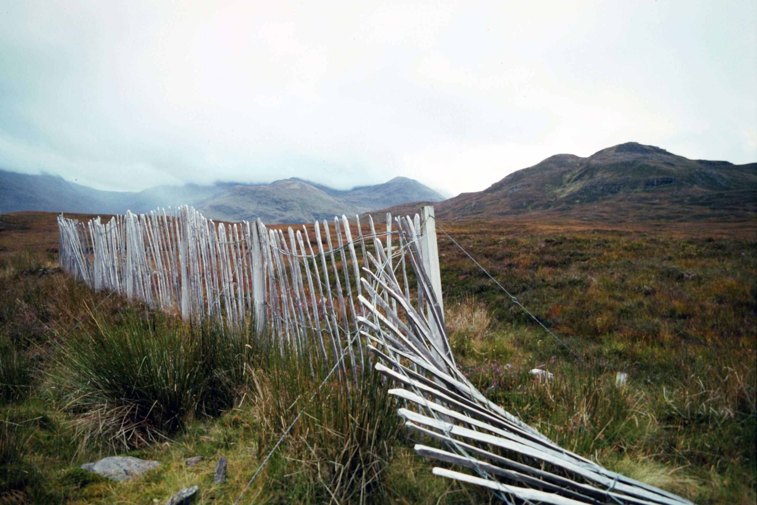 Rural landscape in the Scottish Highlands featuring a rustic white wooden fence and rolling hills.